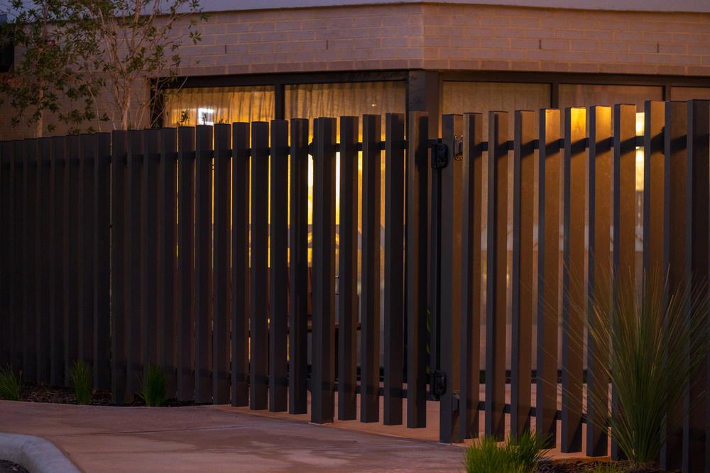 Dark vertical blade fencing lit at dusk in front of a building